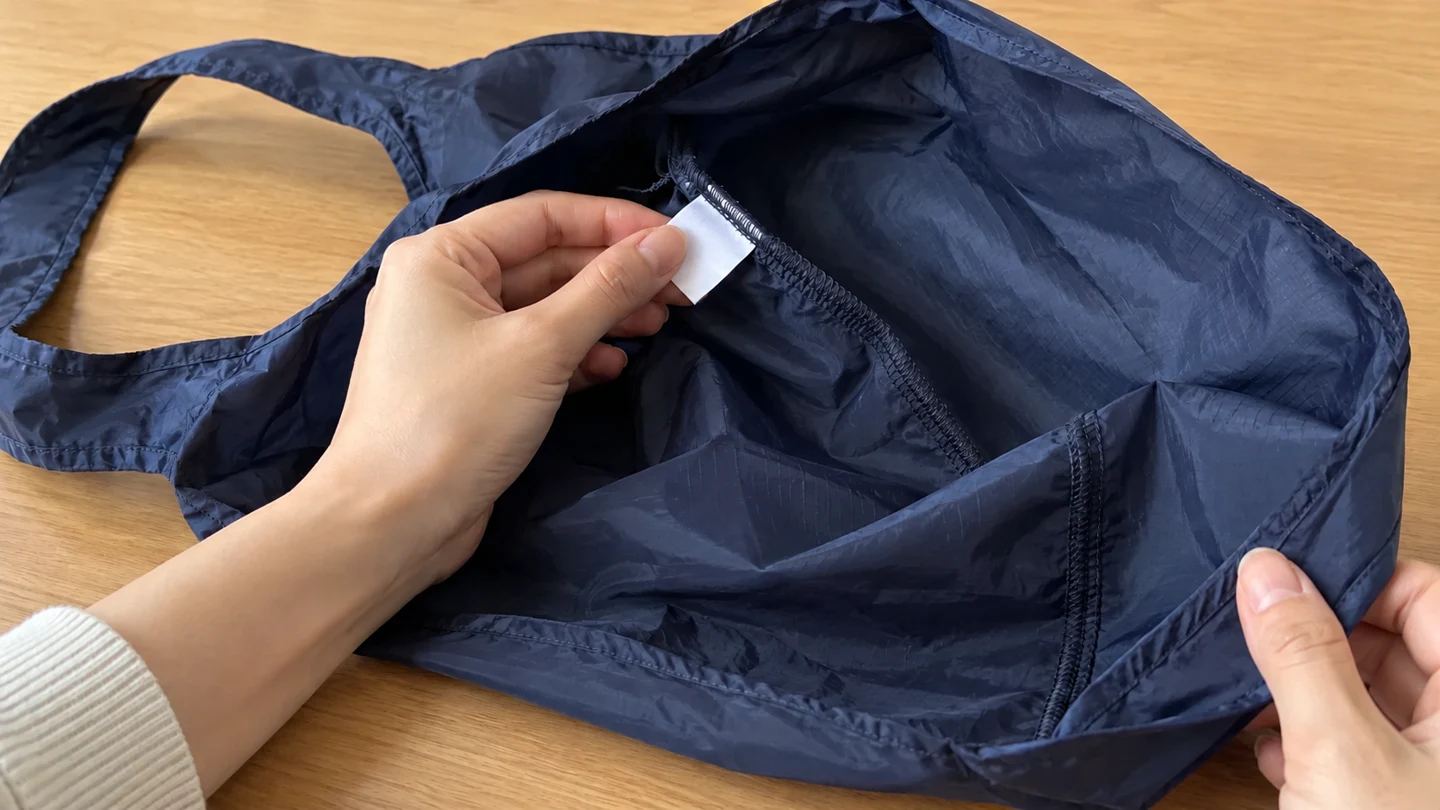 布製バッグのタグ位置と縫い目を確認する説明用イメージ。タグは白紙で実際の洗濯表示を示すものではありません